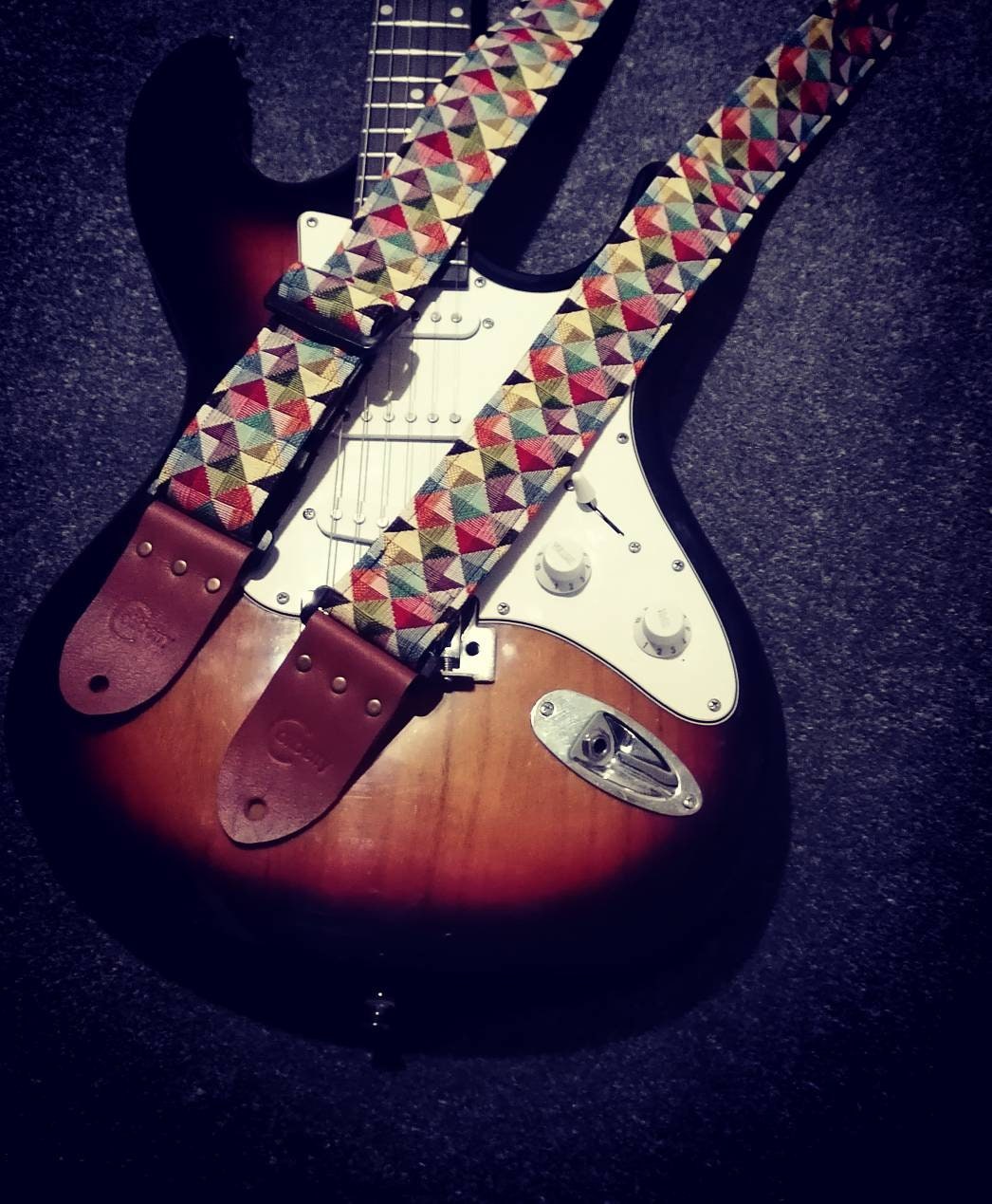 Handmade guitar strap. Multicolored 3D Squares design with black Seatbelt backing. Finished with Montana Hazelnut colour Real Leather ends.