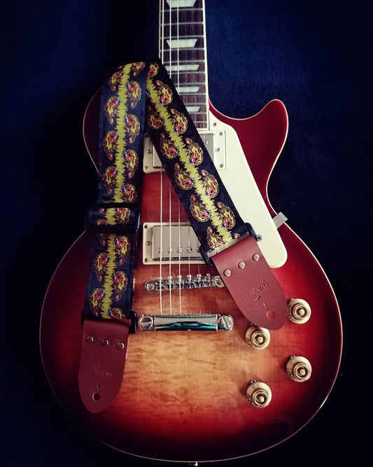 Handmade guitar strap. Yellow and Orange Fireball embroidered skulls ribbon with black seatbelt backing and Montana Hazelnut leather ends.