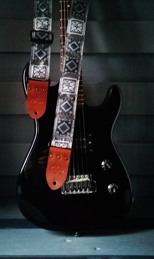 Handmade guitar strap. Grey with geometric design and  seat belt backing. Finished with Montana hazelnut leather ends